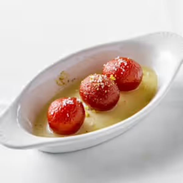 Three gulab jamun, red Indian desserts, in a white dish with syrup and sprinkles.