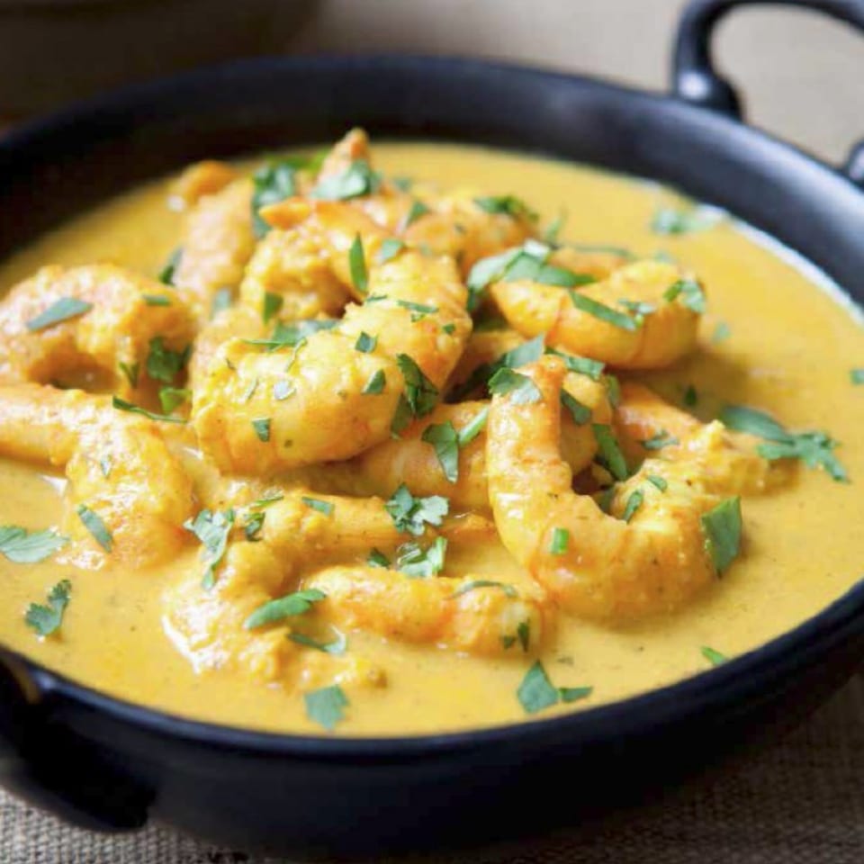 Indian shrimp curry in a black bowl, garnished with fresh green herbs.