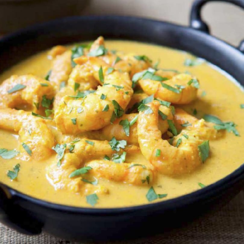Indian shrimp curry in a black bowl, garnished with fresh green herbs.