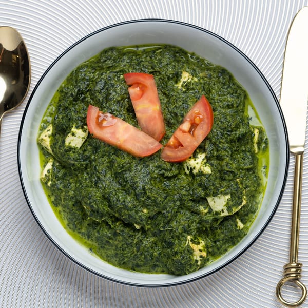 Palak Paneer, an Indian spinach and cheese dish, garnished with tomato slices in a white bowl.