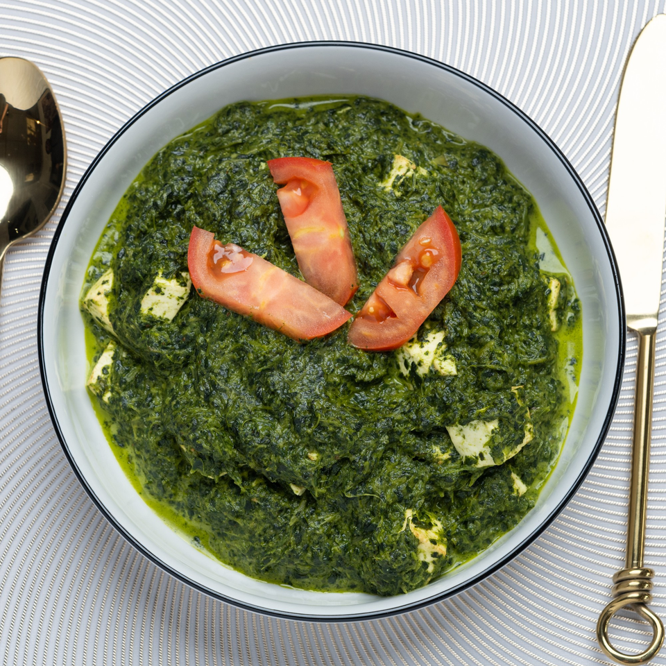 Palak Paneer, an Indian spinach and cheese dish, garnished with tomato slices in a white bowl.