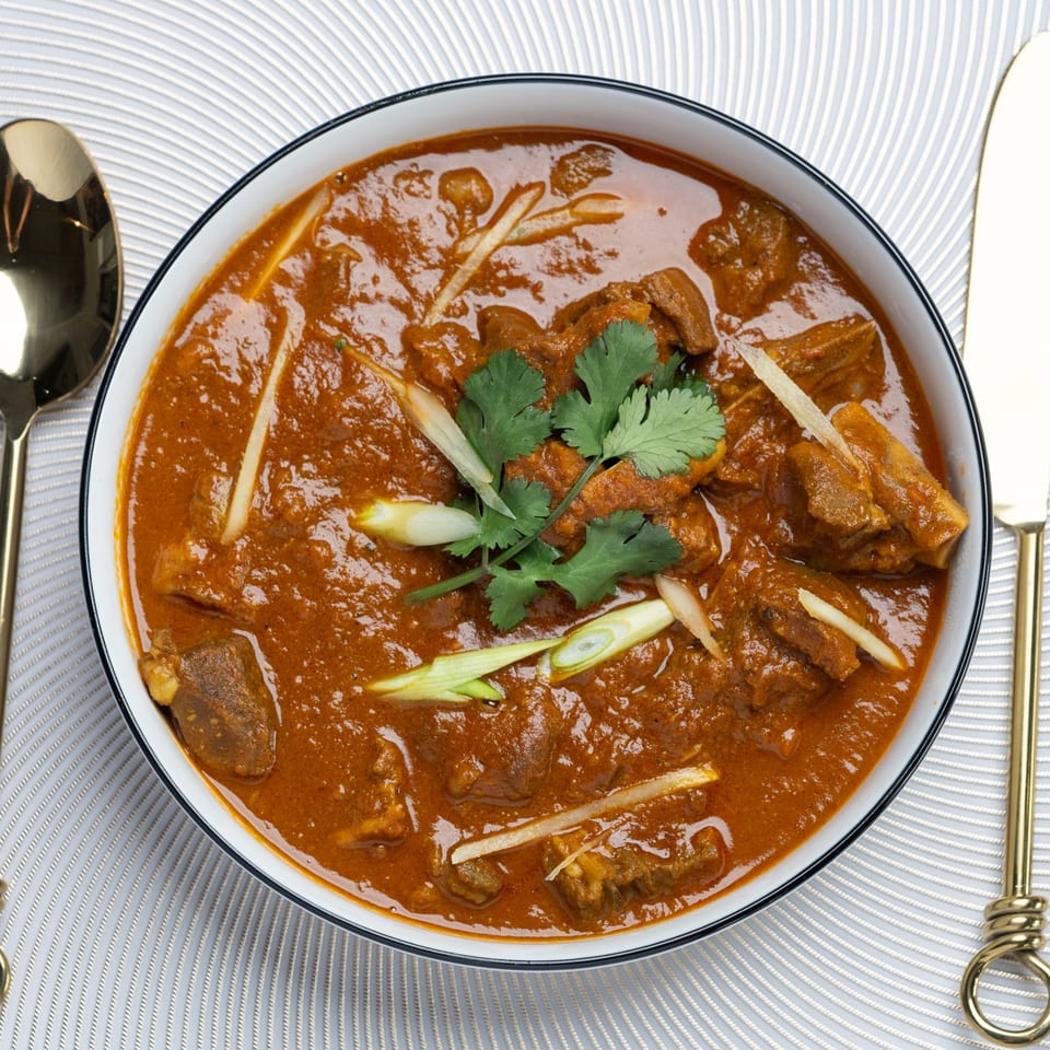Taj Mahal Grill & Bar's Indian lamb curry, garnished with fresh cilantro and ginger, on a textured placemat.