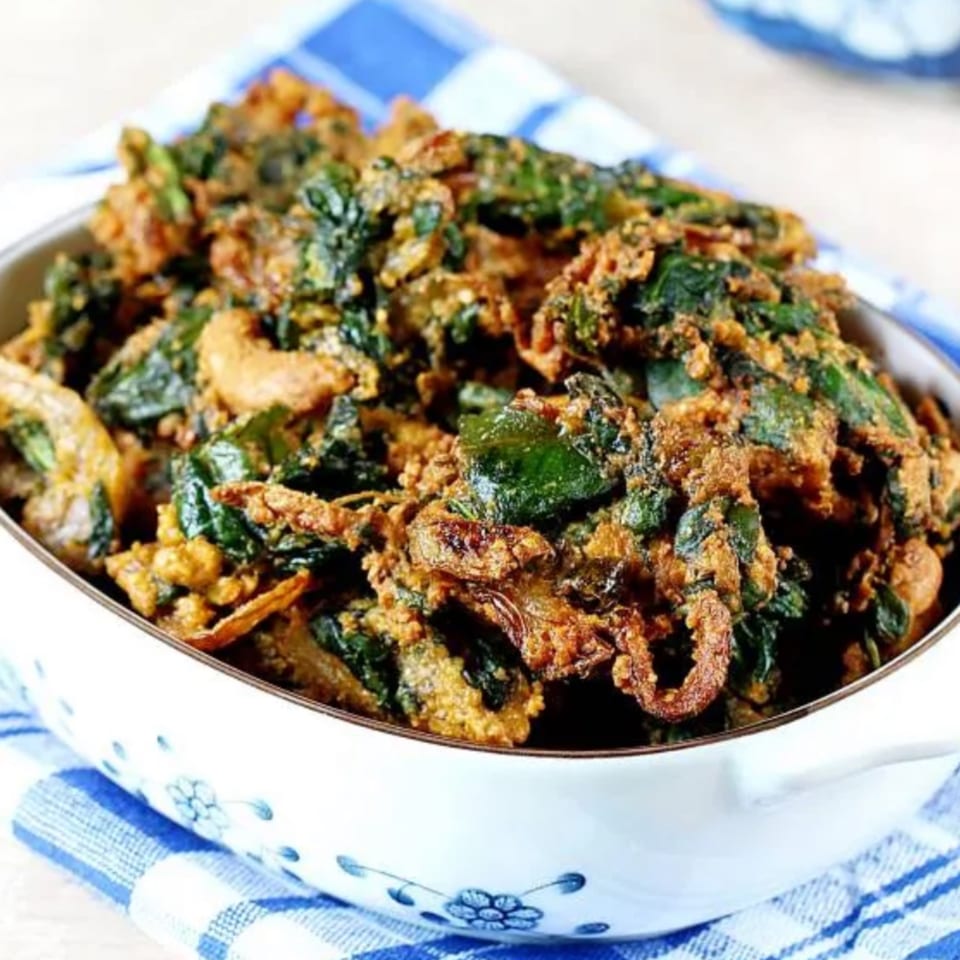 A white bowl filled with crispy, golden-brown Indian spinach pakora sits on a blue and white checkered cloth.
