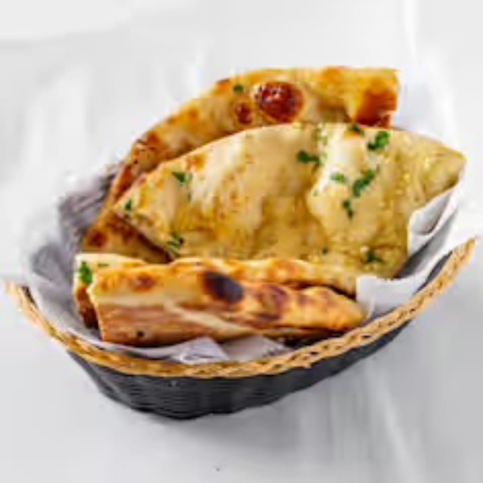 Golden brown naan bread, garnished with herbs, served in a black woven basket with white lining.