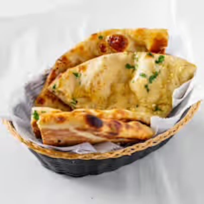 Golden brown naan bread, garnished with herbs, served in a black woven basket with white lining.
