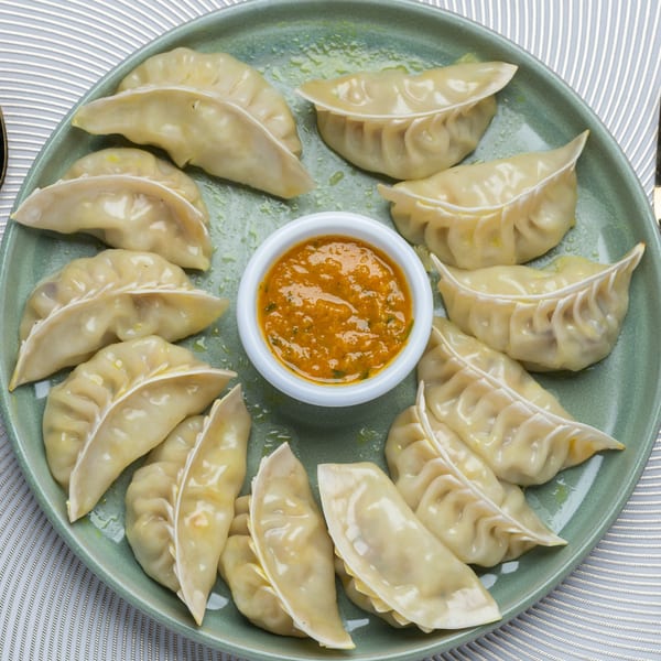 A green plate of Taj Mahal Grill & Bar momos with a small bowl of orange dipping sauce.