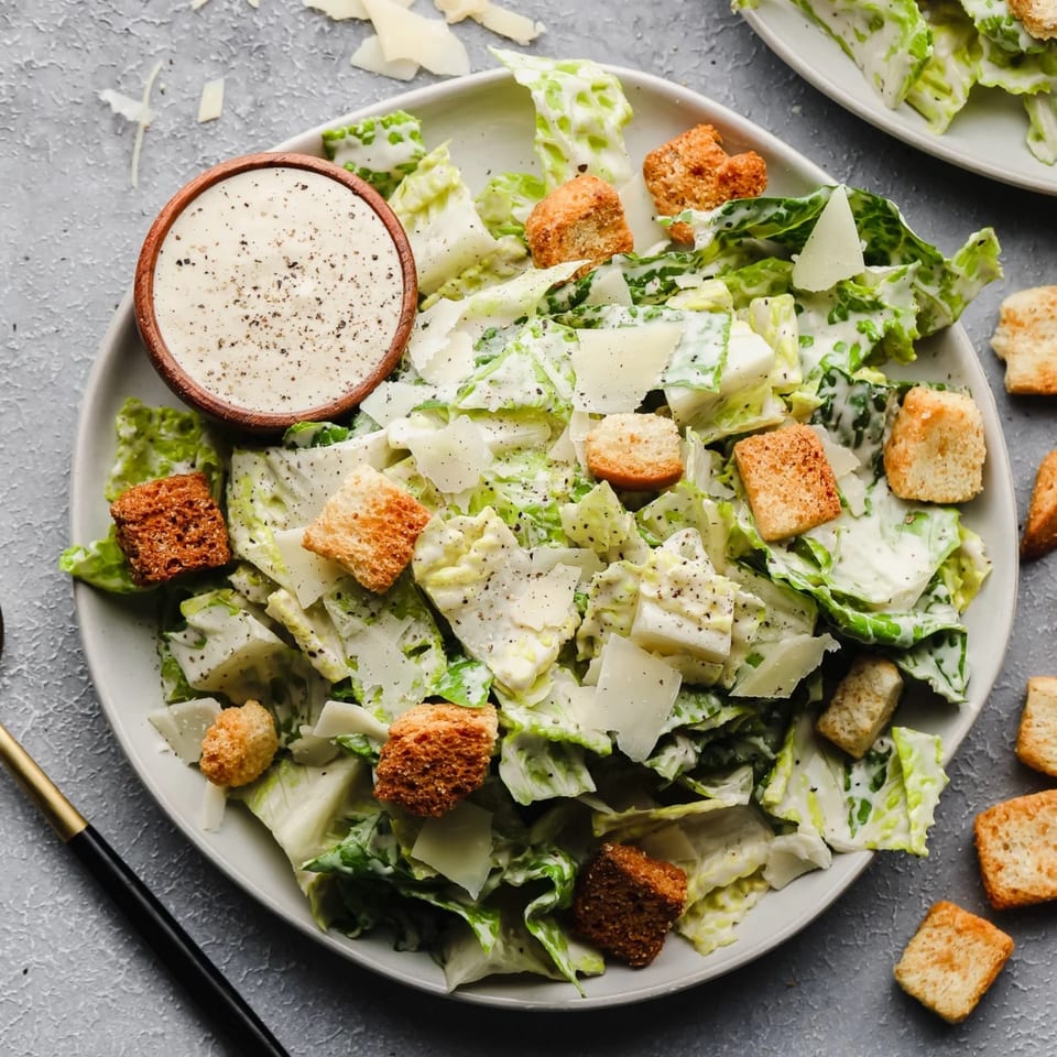 Caesar salad with dressing, croutons, and shaved parmesan on a white plate.