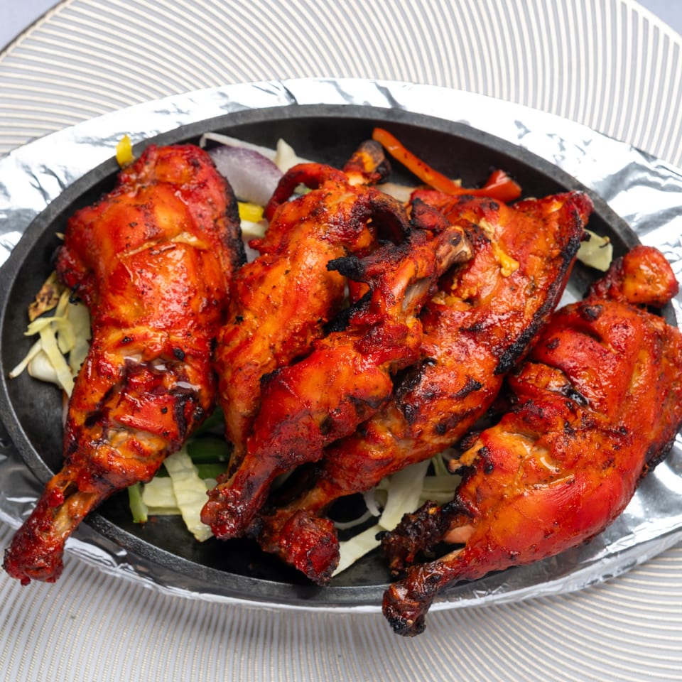Four pieces of Tandoori Chicken, garnished with onions and bell peppers, in a black skillet.