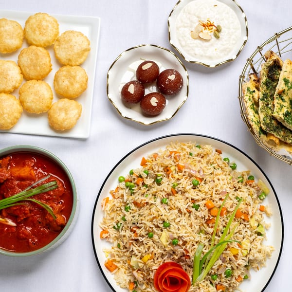 A top-down view of a variety of Indian dishes, including gulab jamun, rice, curry, and naan.