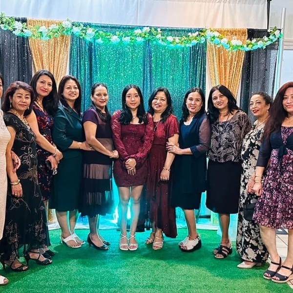 Eleven women in formal attire pose for a group photo in front of a sequined backdrop.