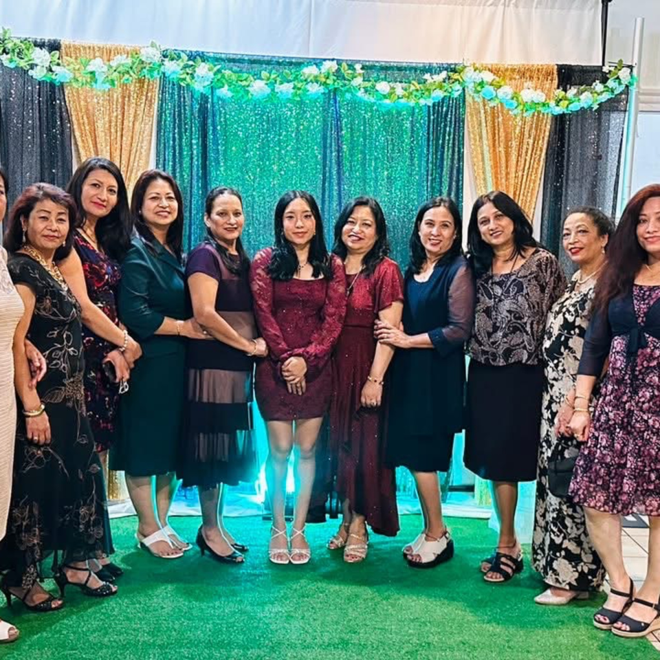 Eleven women in formal attire pose for a group photo in front of a sequined backdrop.
