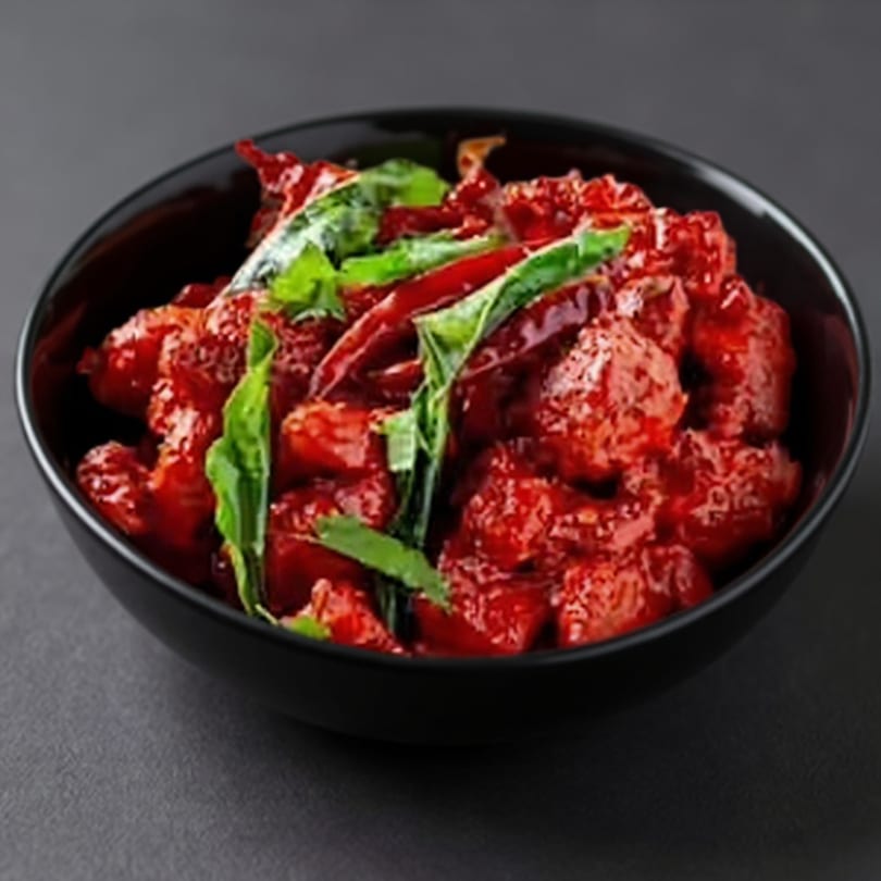 Taj Mahal Grill & Bar's vibrant red Indian chicken dish, garnished with green herbs and red chilies in a black bowl.