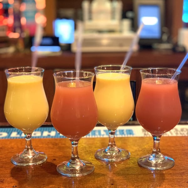 Four colorful Indian drinks, two yellow and two red, in stemmed glasses with straws on a bar.