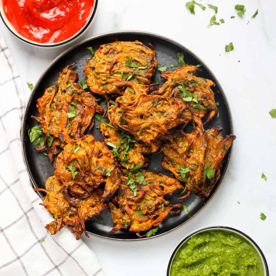 Crispy Indian onion bhaji pakoras garnished with cilantro, served with red and green chutneys.