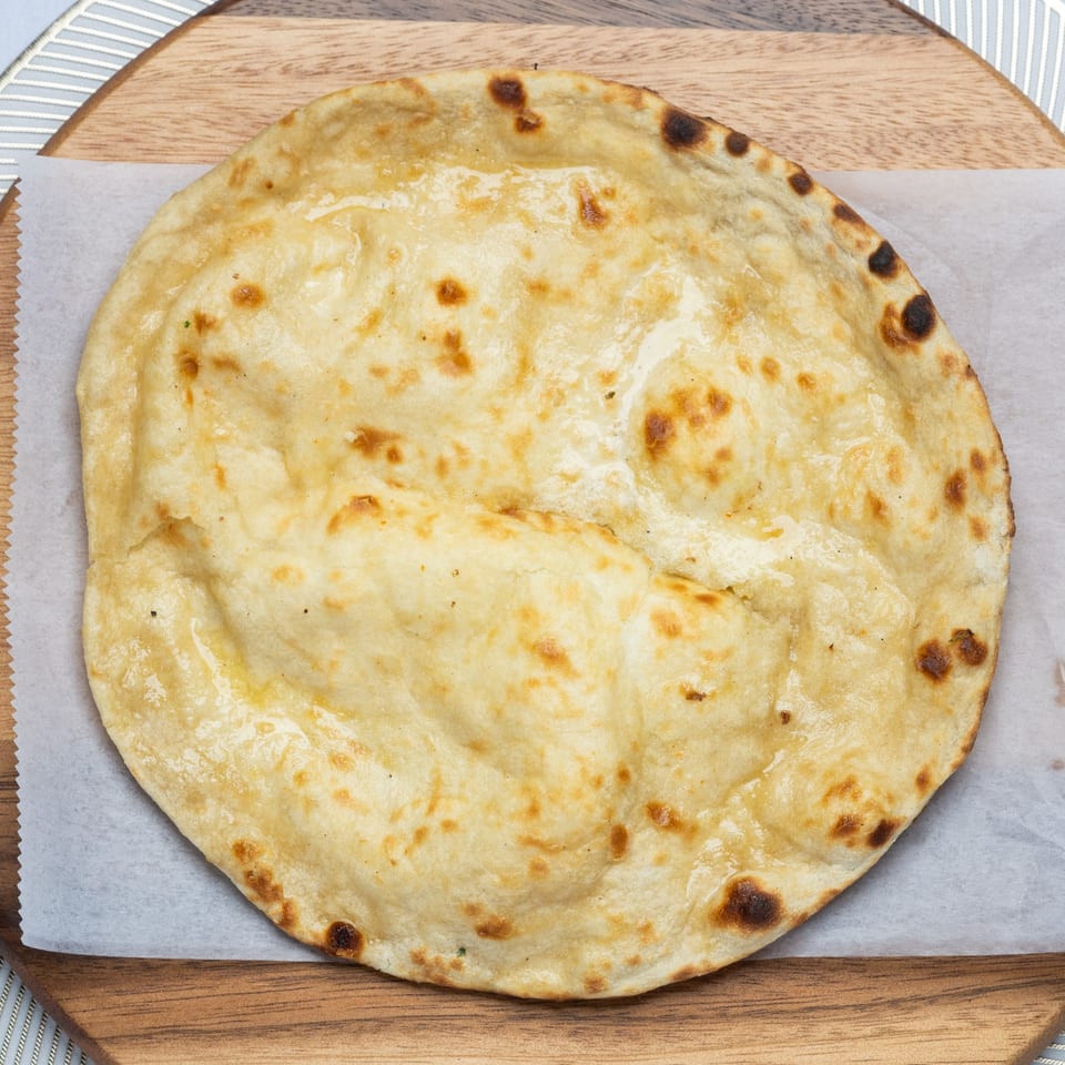 Golden-brown naan bread, lightly charred, rests on parchment paper atop a wooden board.