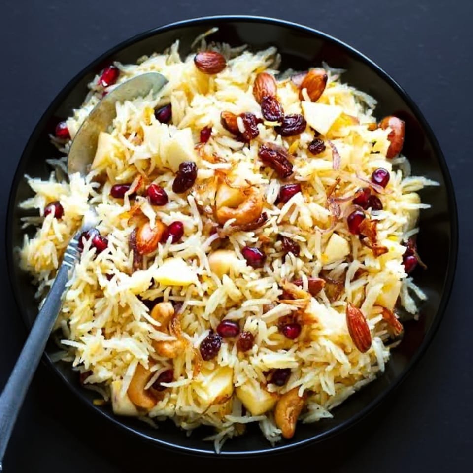 Indian rice pilaf with cashews, almonds, raisins, and pomegranate seeds in a black bowl.