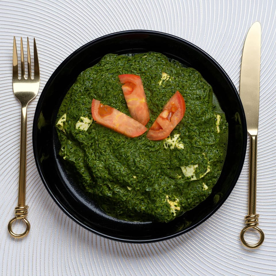 Taj Mahal Grill & Bar's Palak Paneer, a vibrant green spinach dish with paneer and tomato slices.