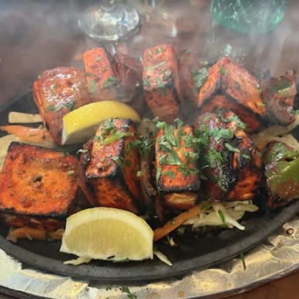 Sizzling Indian paneer tikka with lemon wedges and vegetables on a hot plate.