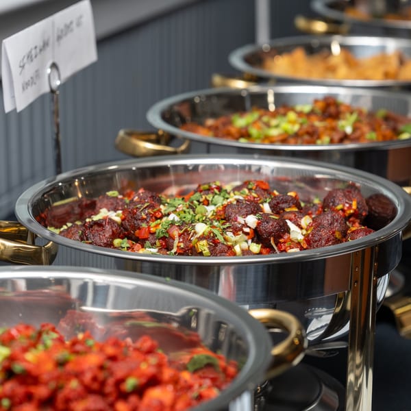 Chafing dishes filled with various Indian dishes, including Manchurian and chili chicken, at a buffet.