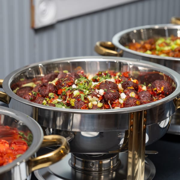 Indian meatballs in a chafing dish, garnished with chopped herbs and vegetables.