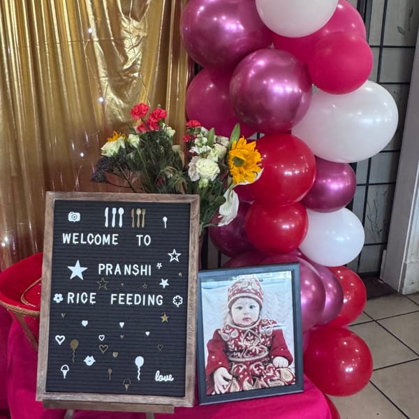 A welcome sign for Pranshi's rice feeding event, with balloons, flowers, and a baby's photo.