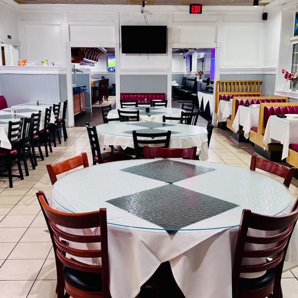 Spacious Taj Mahal Grill & Bar dining room with round tables, white tablecloths, and red booth seating.