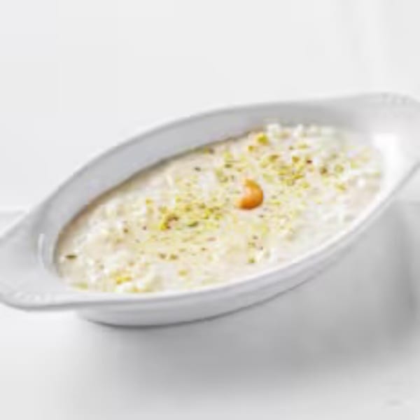 Indian rice pudding, Kheer, topped with chopped pistachios and a cashew, served in a white dish.