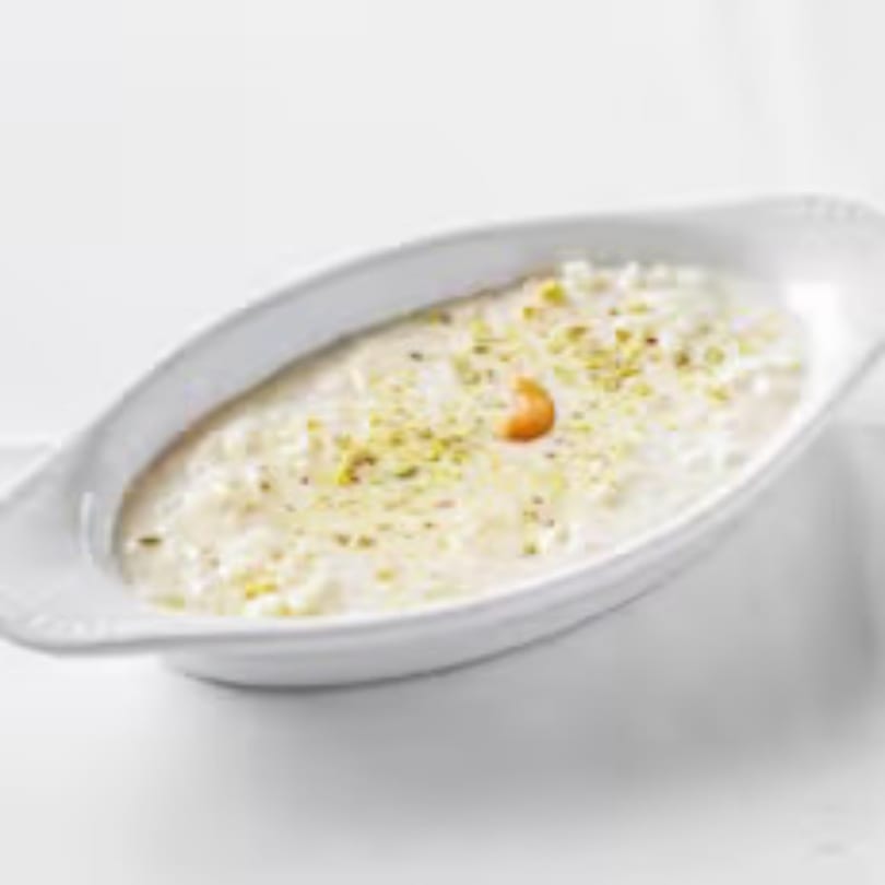 Indian rice pudding, Kheer, topped with chopped pistachios and a cashew, served in a white dish.