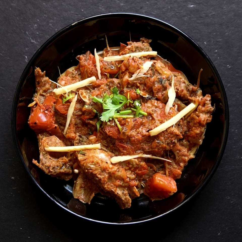 Overhead view of an Indian dish with meat, tomatoes, and cilantro in a black bowl.