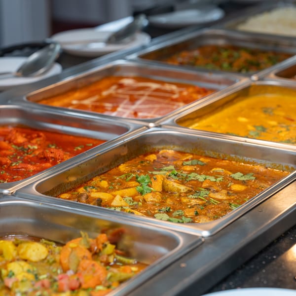 A buffet line with several metal trays filled with various Indian curries and dishes.