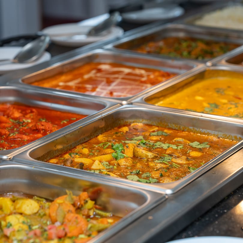 A buffet line with several metal trays filled with various Indian curries and dishes.