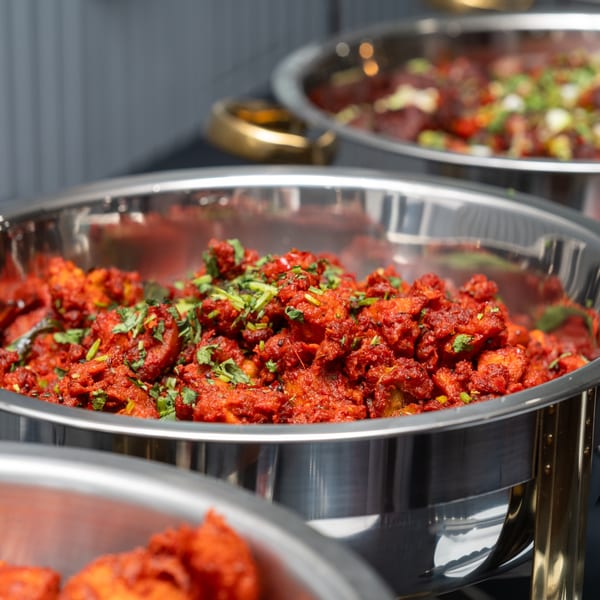 Close-up of vibrant red chicken 65, garnished with fresh cilantro, in a stainless steel chafing dish.