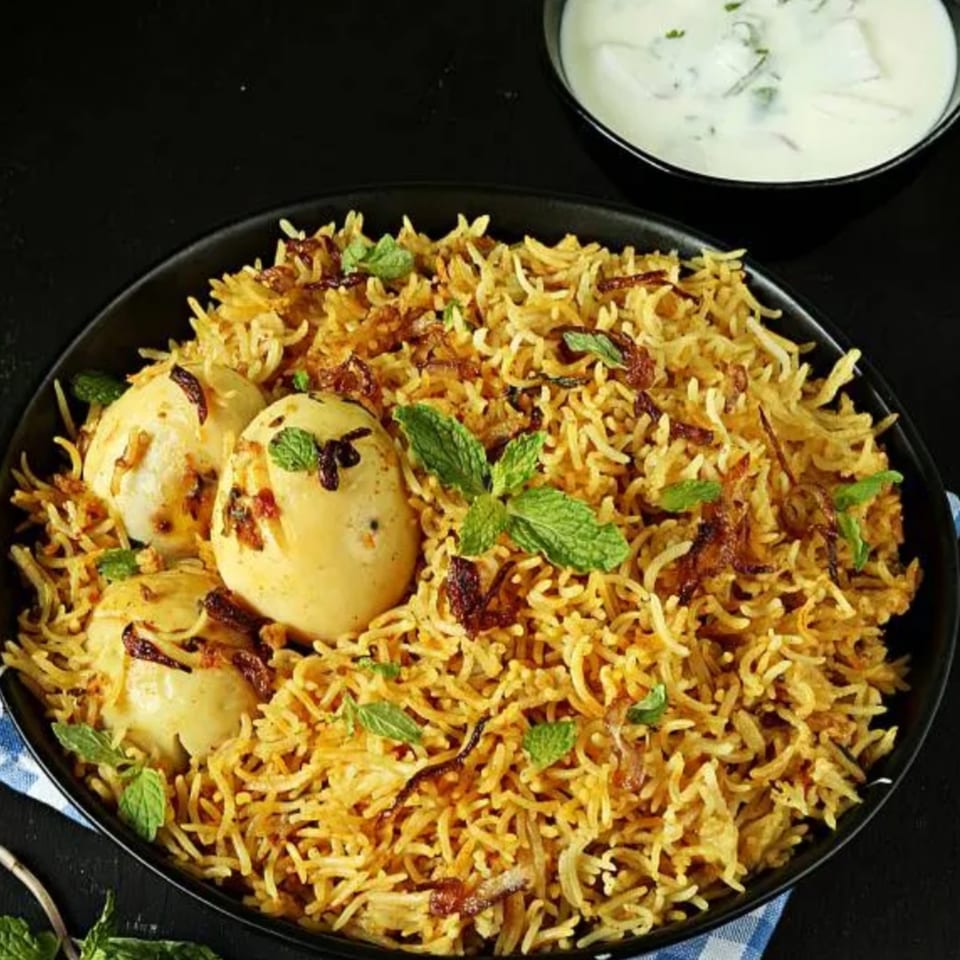 Taj Mahal Grill & Bar's egg biryani, garnished with mint, served with a side of raita.