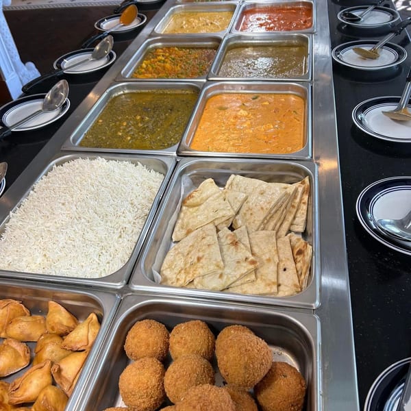 A buffet spread with various Indian dishes including curries, rice, naan, samosas, and fried appetizers.