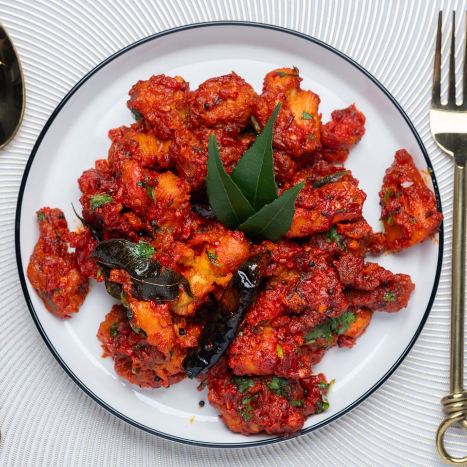Taj Mahal Grill & Bar's Indian chicken dish, vibrant red with green herbs, on a white plate.